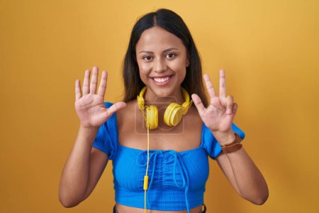 Photo for Hispanic young woman standing over yellow background showing and pointing up with fingers number eight while smiling confident and happy. - Royalty Free Image