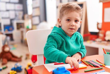 Photo for Adorable caucasian boy preschool student sitting on table drawing on notebook at kindergarten - Royalty Free Image