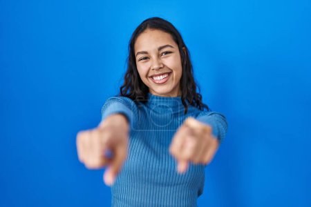 Téléchargez les photos : Jeune femme brésilienne debout sur fond bleu isolé pointant vers vous et la caméra avec les doigts, souriant positif et joyeux - en image libre de droit