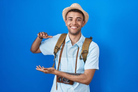 Photo for Brazilian young man holding vintage camera gesturing with hands showing big and large size sign, measure symbol. smiling looking at the camera. measuring concept. - Royalty Free Image