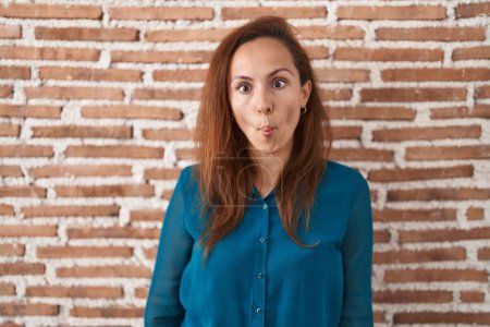 Téléchargez les photos : Femme brune debout sur un mur de briques faisant visage de poisson avec des lèvres, geste fou et comique. expression drôle. - en image libre de droit