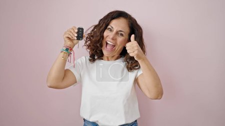 Foto de Mujer hispana de mediana edad sosteniendo la llave de un coche nuevo haciendo un gesto aceptable sobre un fondo rosa aislado - Imagen libre de derechos