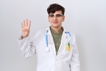 Téléchargez les photos : Jeune homme non binaire portant l'uniforme de médecin et stéthoscope montrant et pointant vers le haut avec les doigts numéro quatre tout en souriant confiant et heureux. - en image libre de droit