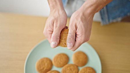 Photo for Young hispanic man breaking cookie with hands at dinning room - Royalty Free Image