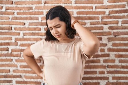 Photo for Young hispanic woman standing over bricks wall suffering of neck ache injury, touching neck with hand, muscular pain - Royalty Free Image