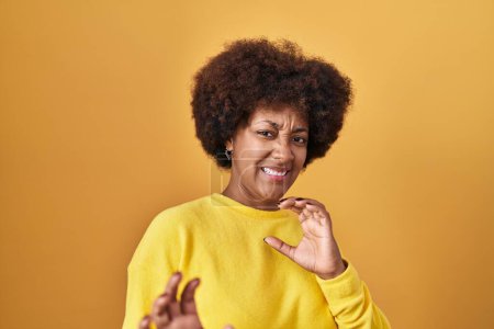 Téléchargez les photos : Jeune femme afro-américaine debout sur fond jaune expression dégoûtée, mécontente et effrayée faisant visage dégoûtant parce que réaction d'aversion. les mains levées - en image libre de droit