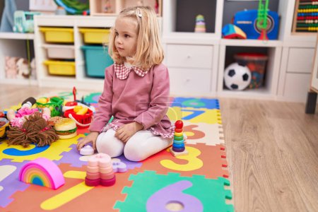 Foto de Adorable chica rubia jugando con juguetes sentados en el suelo en el jardín de infantes - Imagen libre de derechos
