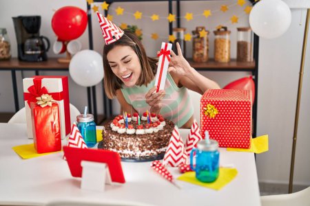 Photo for Young beautiful hispanic woman celebrating online birthday holding gift at home - Royalty Free Image