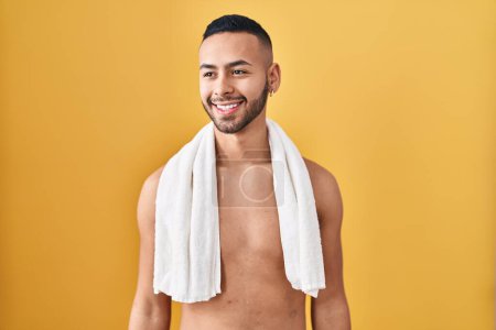 Photo for Young hispanic man standing shirtless with towel looking away to side with smile on face, natural expression. laughing confident. - Royalty Free Image