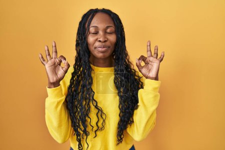 Photo for African woman standing over yellow background relax and smiling with eyes closed doing meditation gesture with fingers. yoga concept. - Royalty Free Image