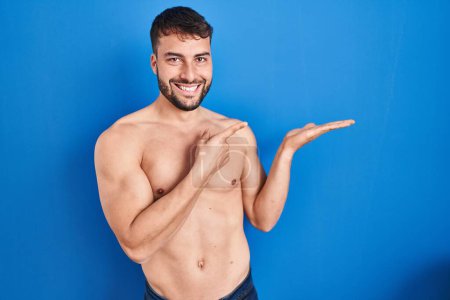 Photo for Handsome hispanic man standing shirtless amazed and smiling to the camera while presenting with hand and pointing with finger. - Royalty Free Image