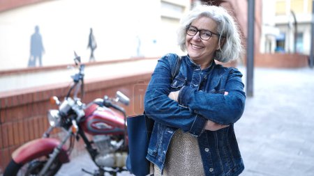 Téléchargez les photos : Femme d'âge moyen avec les cheveux gris souriant avec les bras croisés à la rue - en image libre de droit