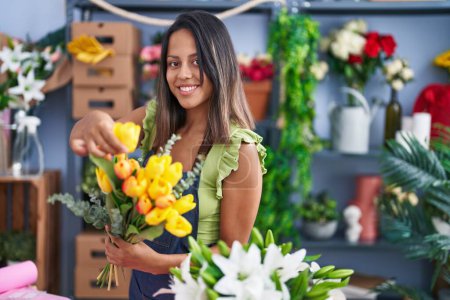 Téléchargez les photos : Jeune femme hispanique fleuriste tenant bouquet de fleurs au magasin de fleuriste - en image libre de droit