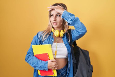 Photo for Young blonde woman wearing student backpack and holding books very happy and smiling looking far away with hand over head. searching concept. - Royalty Free Image