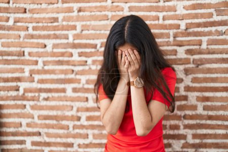 Jeune adolescente debout sur un mur de briques avec une expression triste couvrant le visage avec les mains tout en pleurant. concept de dépression. 