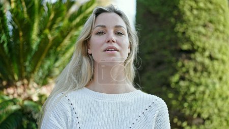 Foto de Young blonde woman standing with serious expression at park - Imagen libre de derechos