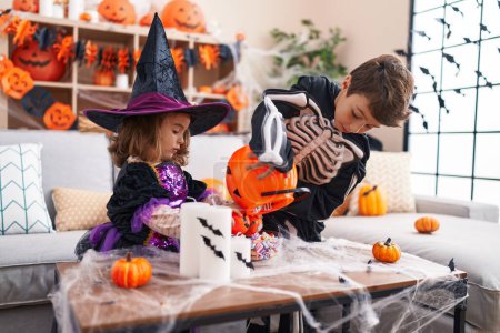 Photo for Adorable boy and girl having halloween party putting candies in pumpkin basket at home - Royalty Free Image