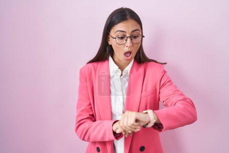 Photo for Young hispanic woman wearing business clothes and glasses looking at the watch time worried, afraid of getting late - Royalty Free Image