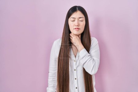 Téléchargez les photos : Jeune femme chinoise debout sur fond rose touchant le cou douloureux, mal de gorge pour la grippe, la motte et l'infection - en image libre de droit