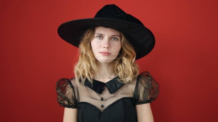 Photo for Young blonde woman wearing witch costume standing with relaxed expression over isolated red background - Royalty Free Image