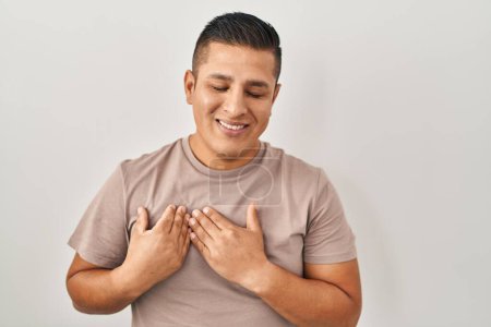 Photo for Hispanic young man standing over white background smiling with hands on chest with closed eyes and grateful gesture on face. health concept. - Royalty Free Image