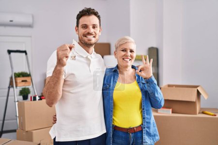 Photo for Hispanic mother and son holding keys of new home doing ok sign with fingers, smiling friendly gesturing excellent symbol - Royalty Free Image