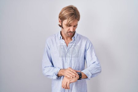 Foto de Hombre caucásico con bigote de pie sobre fondo blanco comprobar el tiempo en reloj de pulsera, relajado y seguro - Imagen libre de derechos
