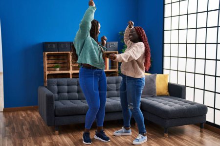 Foto de Afro-americanas amigas sonriendo confiadas bailando en casa - Imagen libre de derechos
