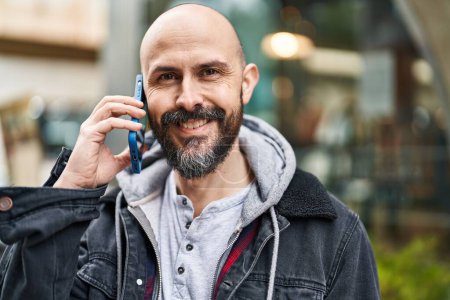 Téléchargez les photos : Jeune chauve souriant confiant parler sur le smartphone à la rue - en image libre de droit