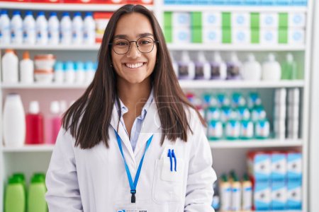 Téléchargez les photos : Jeune belle femme hispanique pharmacien souriant confiance debout à la pharmacie - en image libre de droit