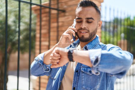 Photo for Young hispanic man talking on the smartphone looking watch at street - Royalty Free Image
