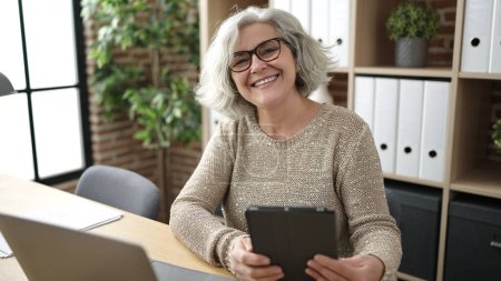 Téléchargez les photos : Middle age woman with grey hair business worker using touchpad and laptop at office - en image libre de droit
