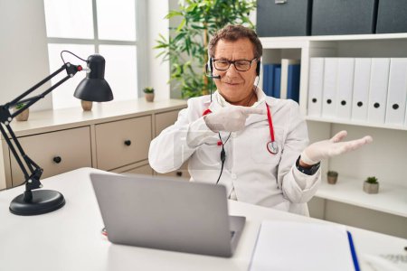 Photo for Senior doctor man working on online appointment amazed and smiling to the camera while presenting with hand and pointing with finger. - Royalty Free Image