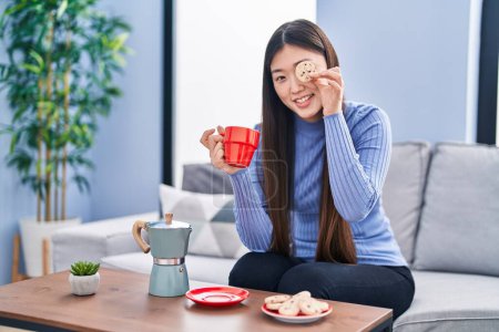 Foto de Mujer china desayunando sosteniendo galletas sobre el ojo en casa - Imagen libre de derechos