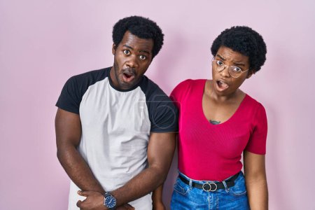 Foto de Joven pareja afroamericana de pie sobre fondo rosa en la cara de choque, mirando escéptico y sarcástico, sorprendido con la boca abierta - Imagen libre de derechos