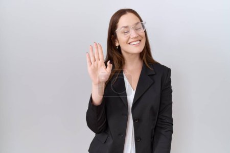 Téléchargez les photos : Belle femme brune portant une veste d'affaires et des lunettes renonçant à dire bonjour heureux et souriant, geste de bienvenue amical - en image libre de droit