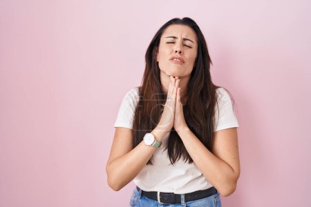 Photo for Young brunette woman standing over pink background begging and praying with hands together with hope expression on face very emotional and worried. begging. - Royalty Free Image