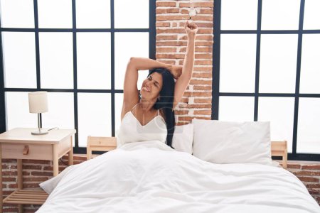 Foto de Middle age hispanic woman waking up stretching arms at bedroom - Imagen libre de derechos