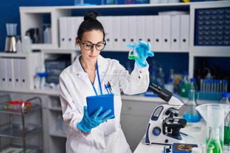 Photo for Young caucasian woman scientist using touchpad holding test tube at laboratory - Royalty Free Image