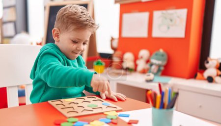 Photo for Adorable caucasian boy playing with maths puzzle game sitting on table at kindergarten - Royalty Free Image