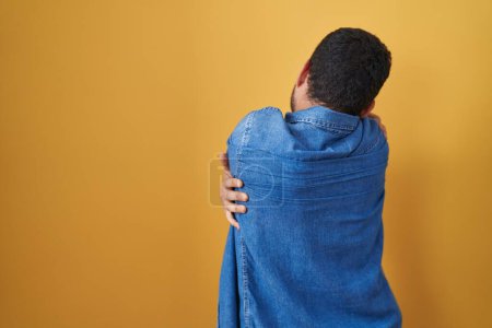 Photo for Hispanic man standing over yellow background hugging oneself happy and positive from backwards. self love and self care - Royalty Free Image