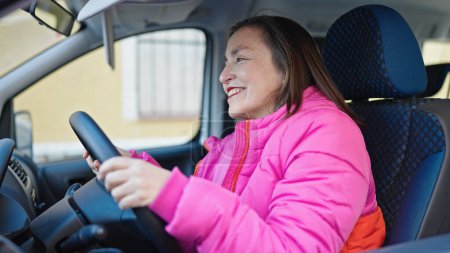 Téléchargez les photos : Femme hispanique mature avec les cheveux gris souriant voiture de conduite confiante à la rue - en image libre de droit