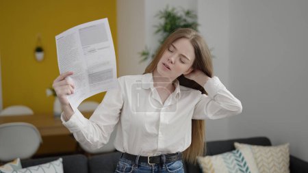 Téléchargez les photos : Jeune femme blonde utilisant des papiers comme un handfan souffrant de chaud à la maison - en image libre de droit