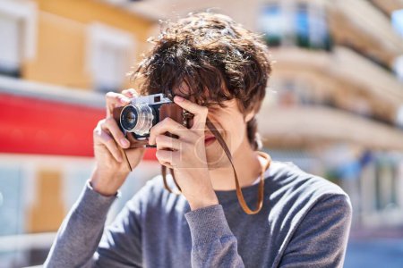 Téléchargez les photos : Jeune homme hispanique souriant confiant en utilisant une caméra vintage à la rue - en image libre de droit