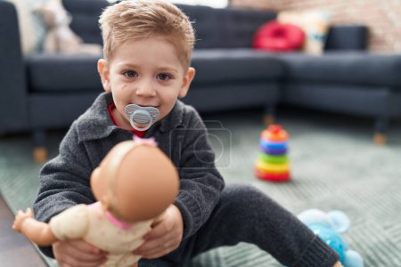Téléchargez les photos : Adorable garçon caucasien jouant avec bébé poupée assis sur le sol à la maison - en image libre de droit
