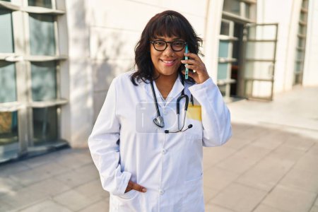 Photo for Young beautiful latin woman doctor smiling confident talking on smartphone at hospital - Royalty Free Image