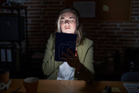 Photo for Blonde caucasian woman working at the office at night touching painful neck, sore throat for flu, clod and infection - Royalty Free Image