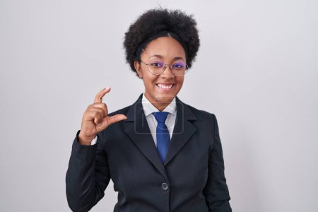 Téléchargez les photos : Belle femme africaine aux cheveux bouclés portant une veste d'affaires et des lunettes geste souriant et confiant avec la main faisant signe de petite taille avec les doigts à la recherche et la caméra. concept de mesure. - en image libre de droit