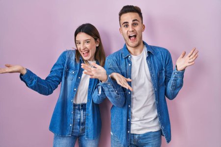 Téléchargez les photos : Jeune couple hispanique debout sur fond rose célébrant fou et étonné pour le succès avec les bras levés et les yeux ouverts hurlant excités. concept gagnant - en image libre de droit