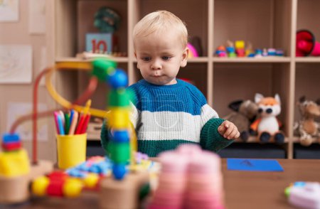 Foto de Adorable chico caucásico jugando con juguetes sentados en la mesa en el jardín de infantes - Imagen libre de derechos